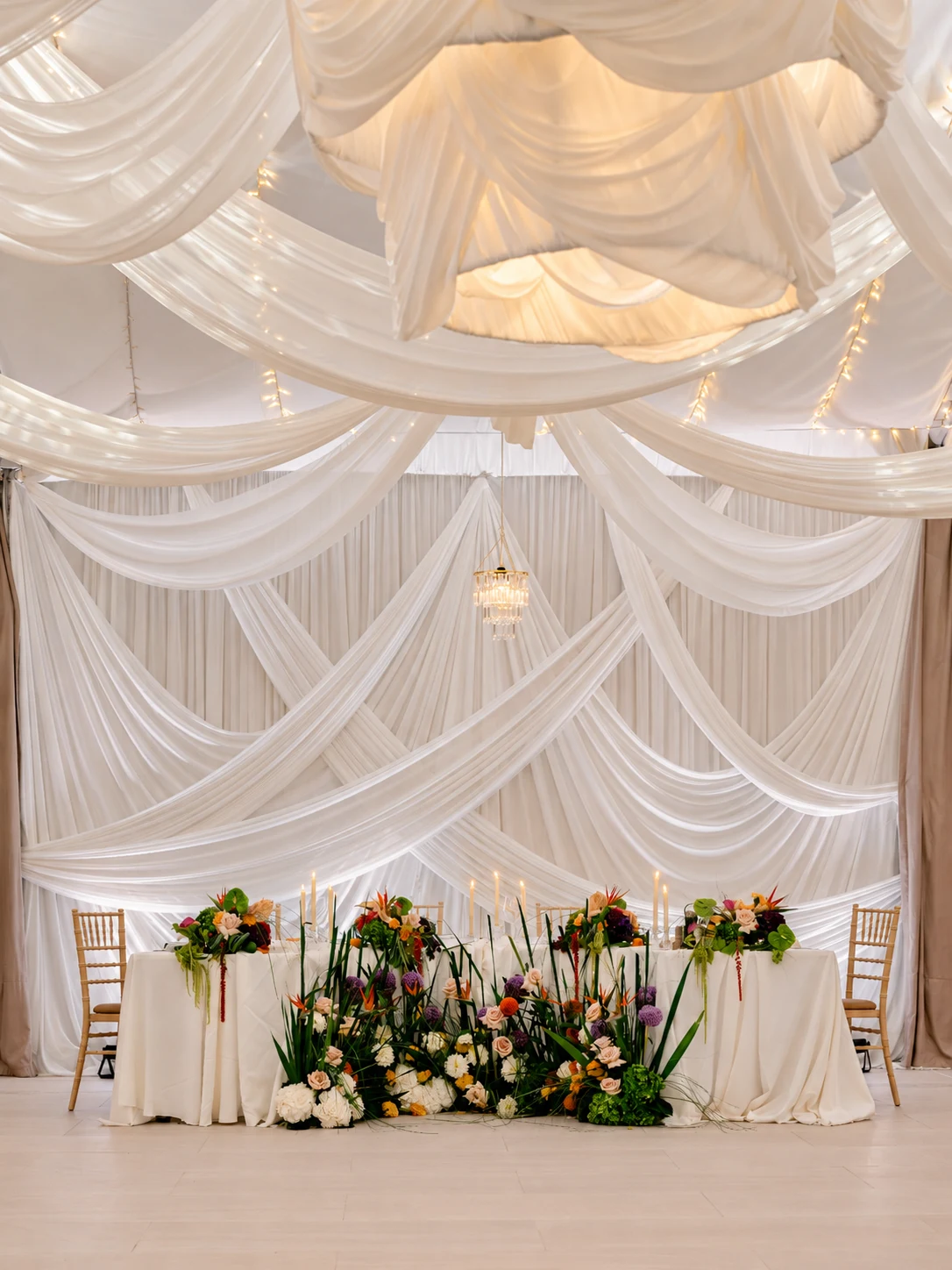 Head table and white drapes in the wedding marquee